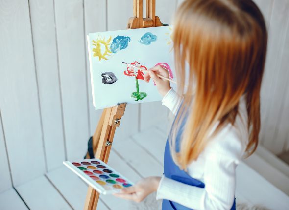 Cute little girl in a blue apron. Child painting at home